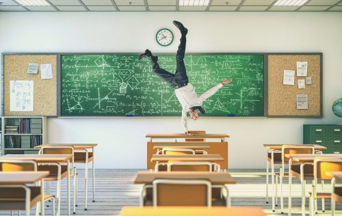 Upside-down teacher balancing on a desk inside a school classroom.
